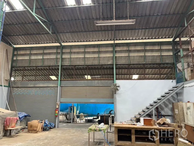 货栈 出租在Khlong Sam Wa, Bangkok - 宽幅卷帘门入口，开阔地面空间与通往夹层的楼梯。