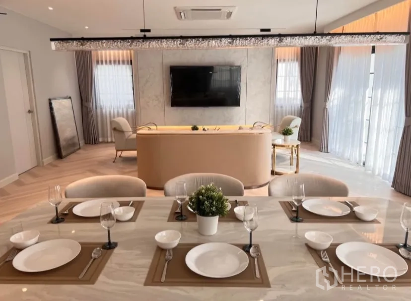 Detached House for rent in Bang Phli, Samut Prakan - Close-up of dining table set with tableware, looking toward the TV wall and curved sofa.