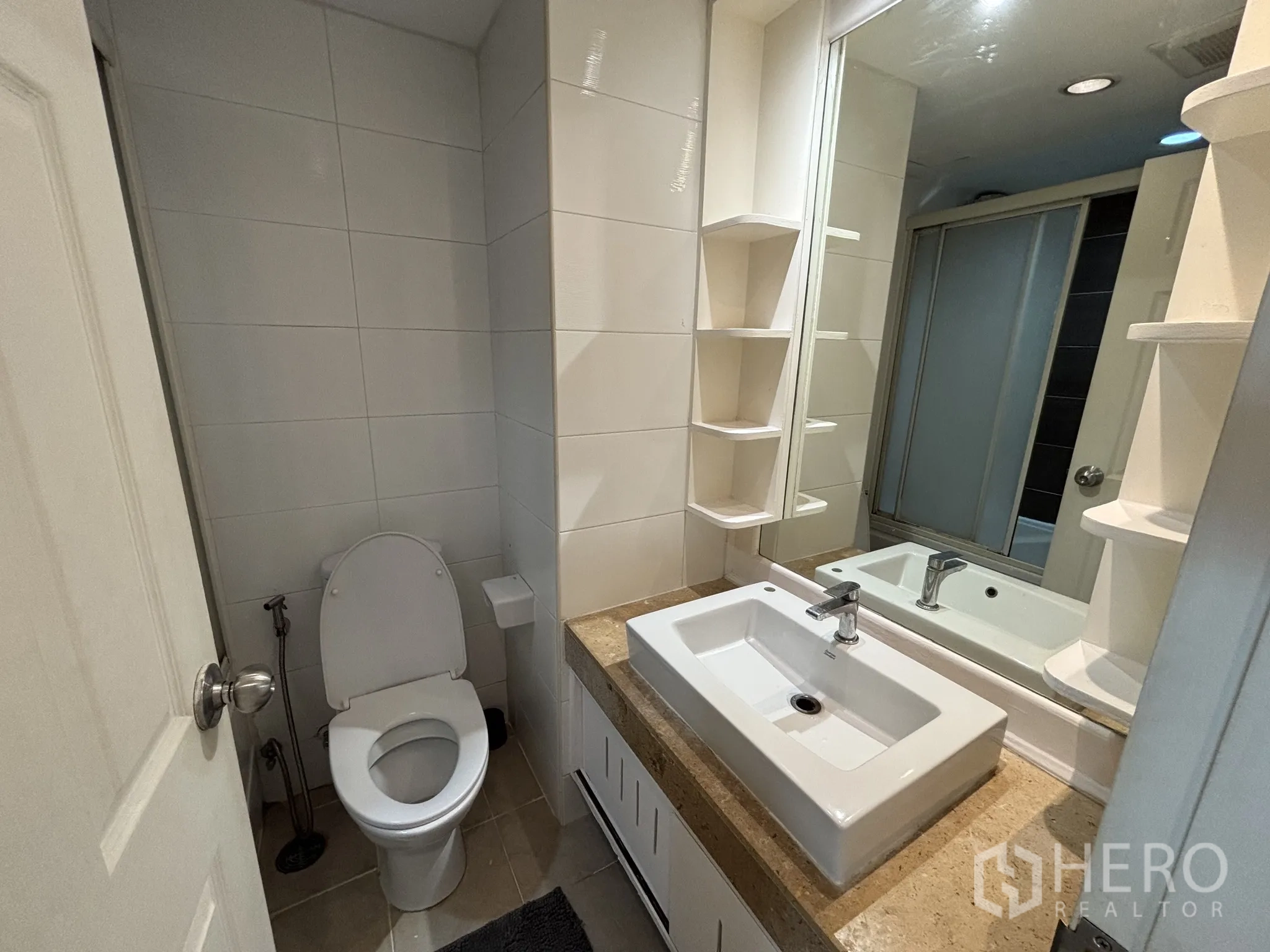 Condominium for rent or sale in Watthana, Bangkok - Modern bathroom with large mirror, square basin, storage shelves and white wall tiles.