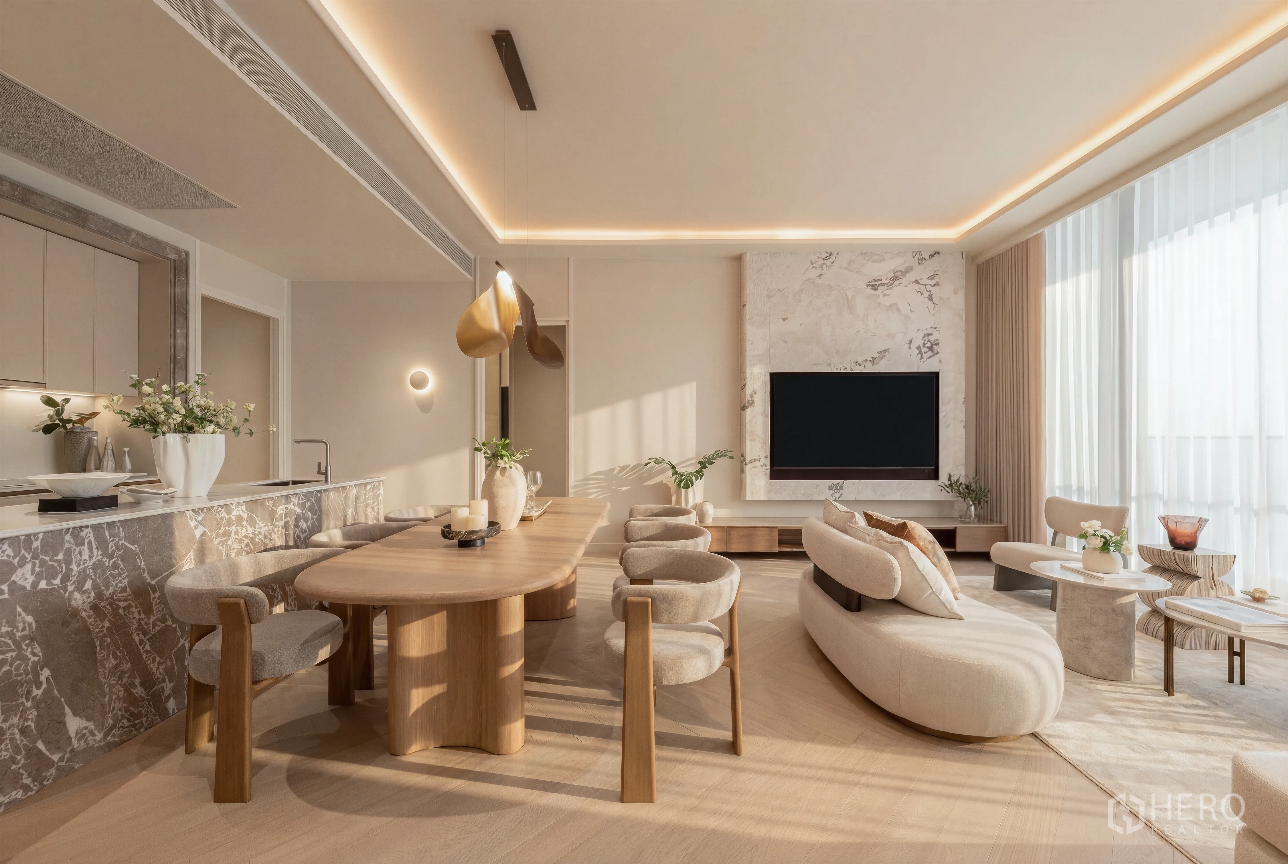 Condominium for sale in Khlong Toei, Bangkok - Sunlit open-plan living and dining area with a marble TV feature wall, curved sofa, stone kitchen island, wood dining table, and floor-to-ceiling sheer curtains.
