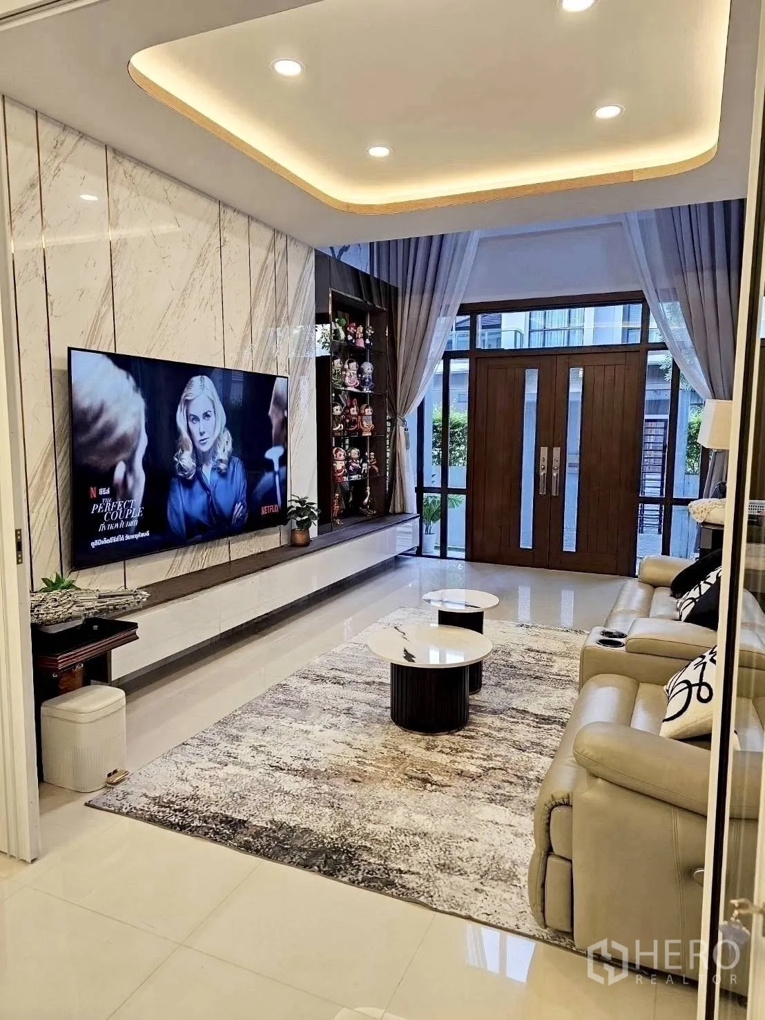 Detached House for rent in Wang Thonglang, Bangkok - Modern living room with marble TV wall, recessed lighting, and a large rug.