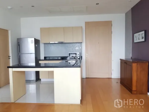 Condominium for rent in Chatuchak, Bangkok - Modern open kitchen featuring a black stone island, light wood cabinets and a stainless‑steel refrigerator.