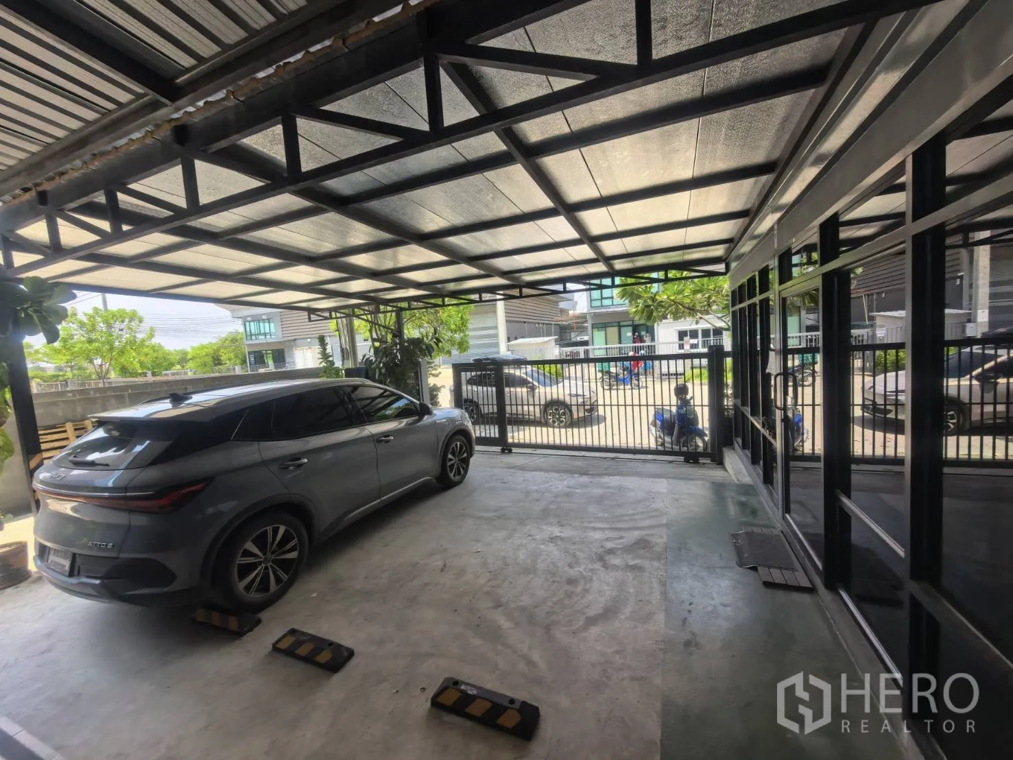 Warehouse for rent in Bang Sao Thong, Samut Prakan - Shaded parking area with car and gated frontage by the glass entrance.