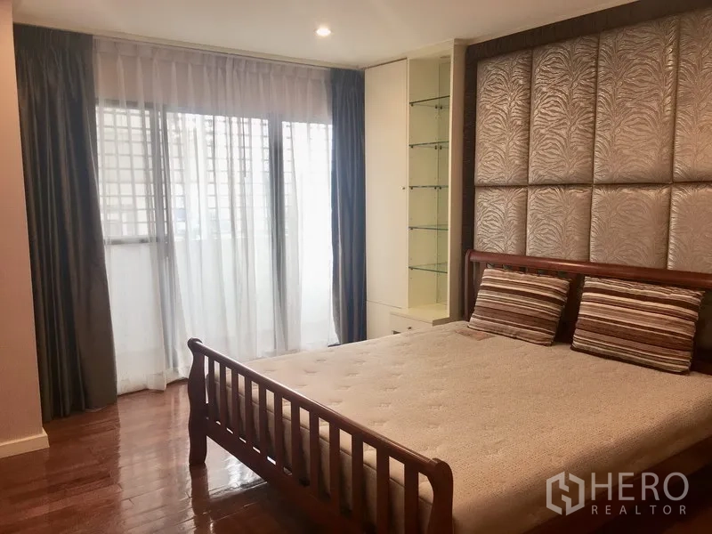 Condominium for rent in Watthana, Bangkok - Second bedroom with wooden bed frame, padded feature wall, display shelving and large windows.