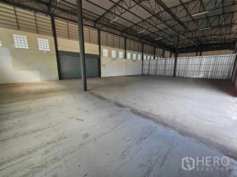 Warehouse for rent in Bang Bua Thong, Nonthaburi - Wide open warehouse floor with metal truss ceiling, natural light panels and a loading roller door.
