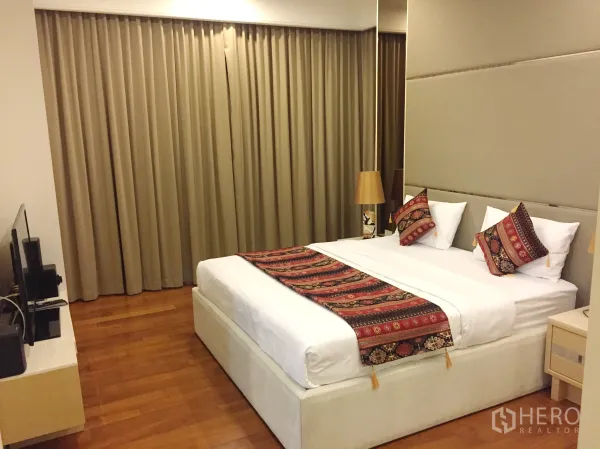 Condominium for rent in Pathum Wan, Bangkok - Spacious master bedroom with large bed, TV console and full-length drapes.