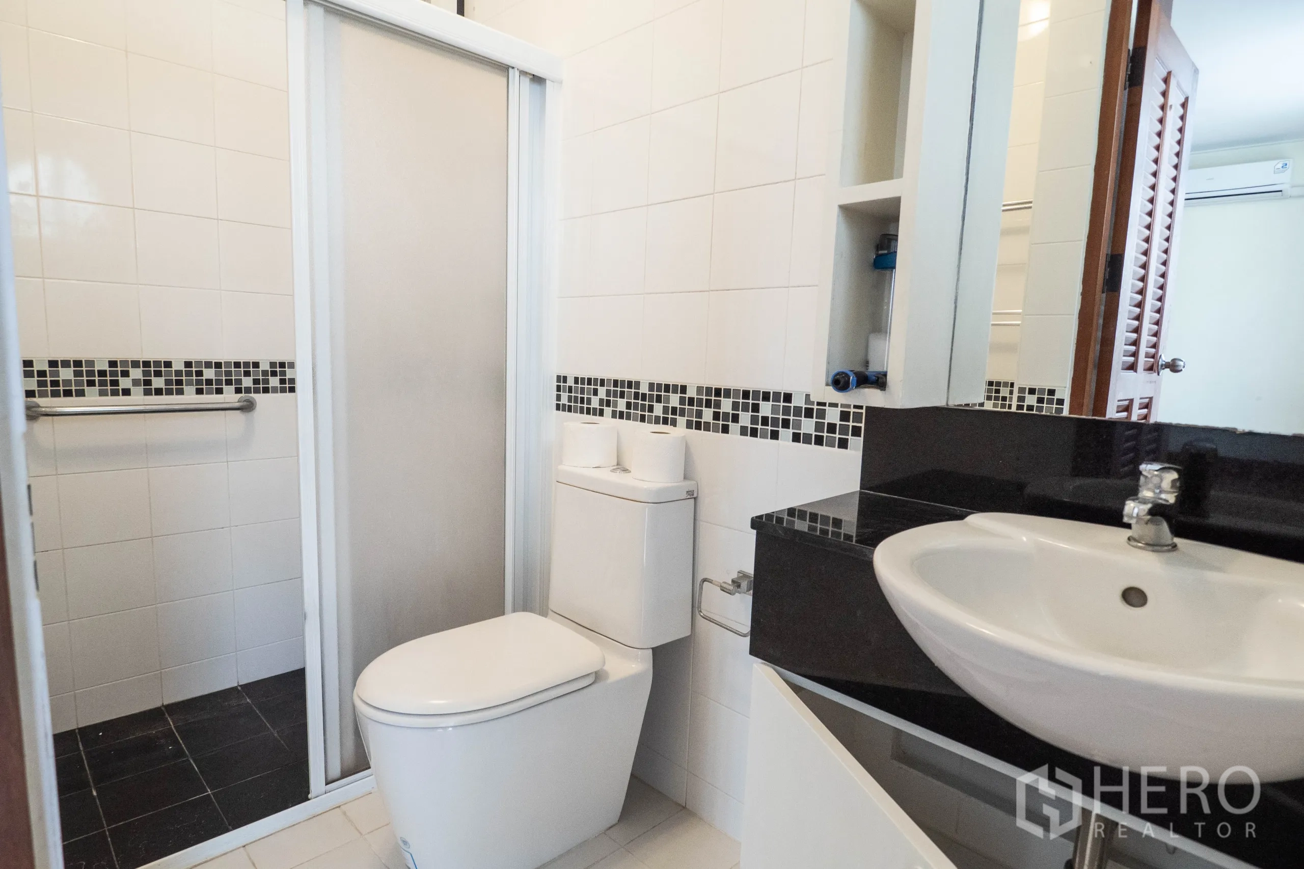 Townhouse for rent in Khlong Toei, Bangkok - White-tiled bathroom with mosaic border and sliding glass shower door.