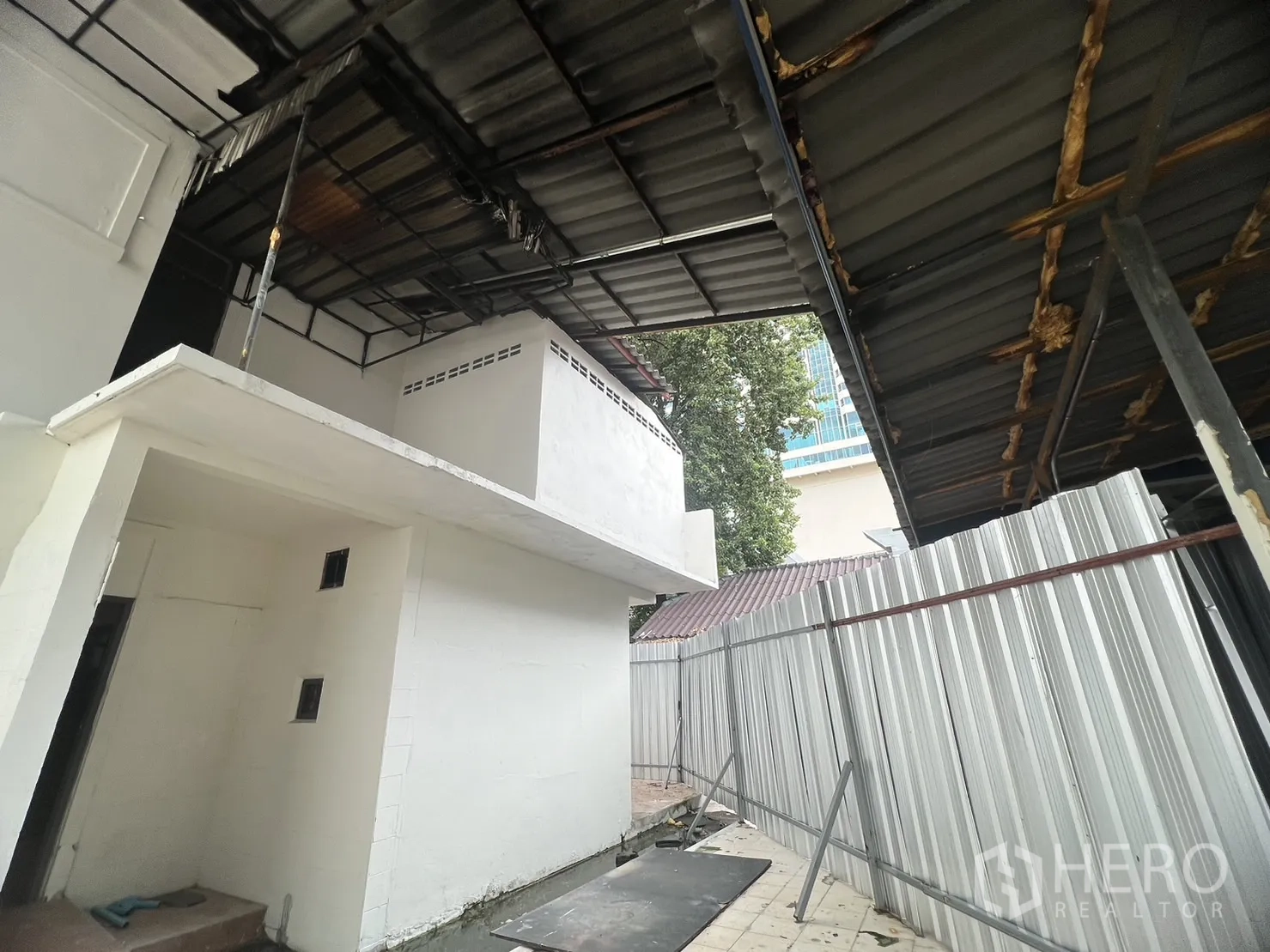 零售空间 出租在Watthana, Bangkok - 建筑侧面带金属雨棚、白墙与波纹围挡。