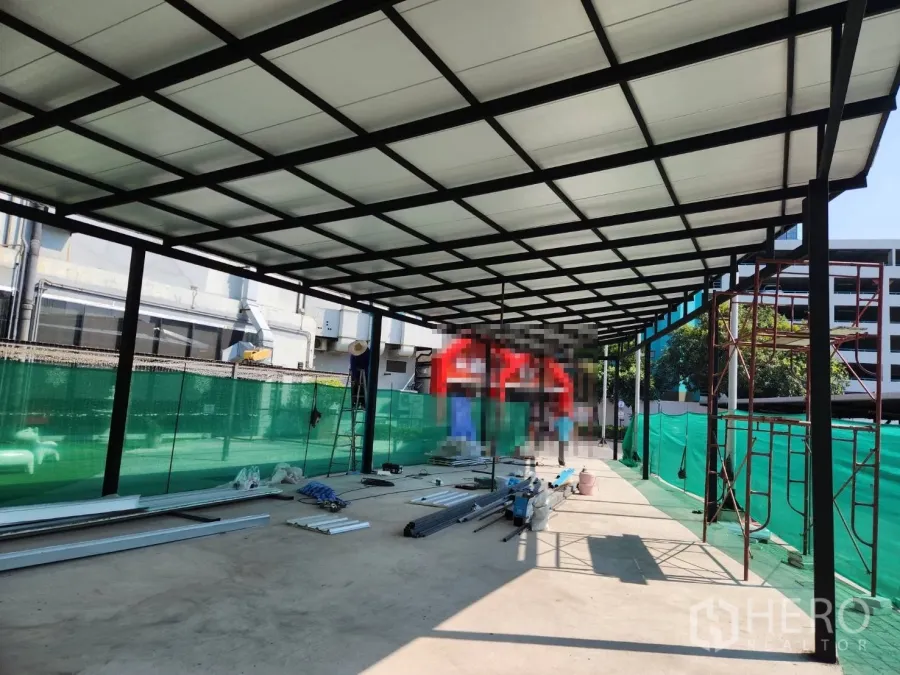 零售空间 出租在Khlong Toei, Bangkok - 位于曼谷Khlong Toei的开放式商铺棚架，钢结构与半透明屋顶在施工中，外围绿色围挡与混凝土地面。