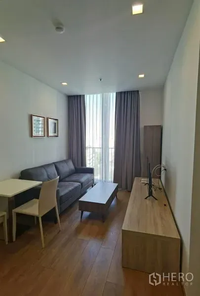 คอนโด ให้เช่าในWatthana, Bangkok - ห้องนั่งเล่นคอนโดสว่าง โปร่ง โซฟาสีเทา ชั้นวางทีวี ชุดโต๊ะกินข้าว พื้นไม้ และหน้าต่างสูงจรดฝ้าเพดานพร้อมผ้าม่าน