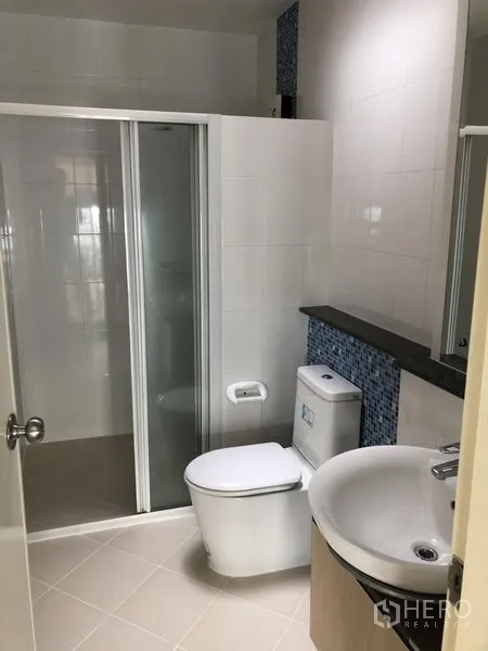 联排别墅 出租在Prawet, Bangkok - 现代浴室，玻璃淋浴间、台上盆与马桶，蓝色马赛克点缀。