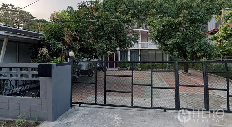Detached House for rent in Phaya Thai, Bangkok - Gated entrance with sliding metal fence, wide paved driveway and mature trees leading to a detached house in Ari.