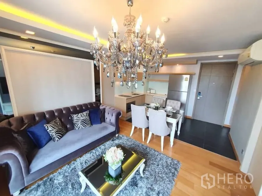 Condominium for rent in Watthana, Bangkok - Open-plan living room with crystal chandelier, velvet sofa, shag rug, and kitchenette in a Bangkok condo.