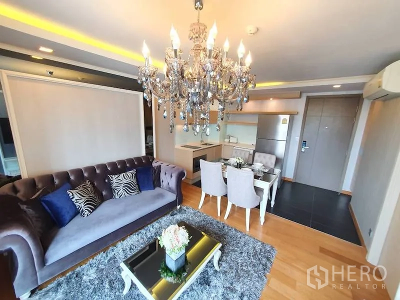 Condominium for rent in Watthana, Bangkok - Open-plan living room with crystal chandelier, velvet sofa, shag rug, and kitchenette in a Bangkok condo.