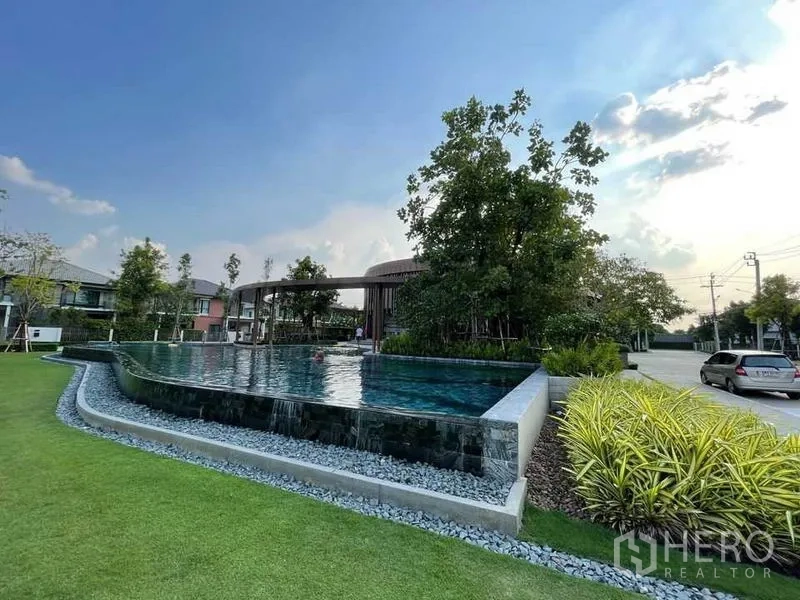 独立式住宅 出售在Pak Kret, Nonthaburi - 度假风无边际泳池，旁有草地与树木。