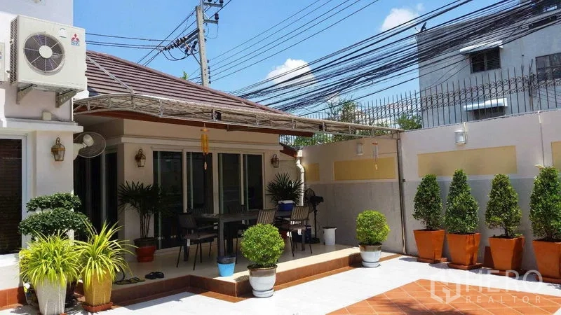 Detached House for sale in Suan Luang, Bangkok - Sunny tiled courtyard with raised terrace and outdoor dining set framed by potted plants.