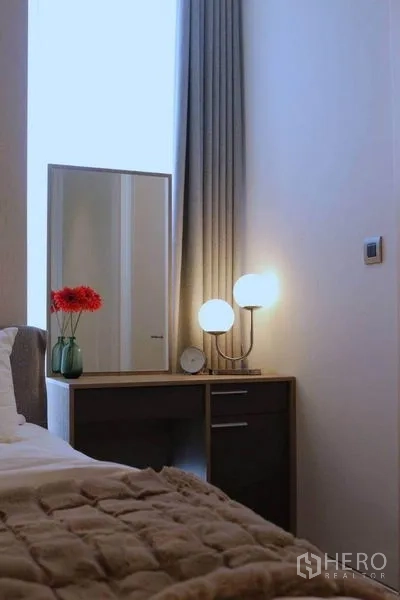 公寓 出租在Watthana, Bangkok - 卧室梳妆台，配镜子、双球形台灯与红花花瓶。