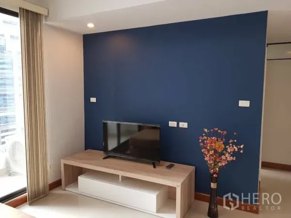 คอนโด ให้เช่าในWatthana, Bangkok - ผนังสีกรมท่าพร้อมทีวีบนชั้นวางไม้และแจกันดอกไม้ ถัดจากประตูกระจกสู่ระเบียง