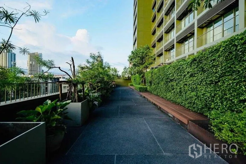 公寓 出租在Watthana, Bangkok - 景观步道，修剪整齐的绿篱、长椅与城市天际线。