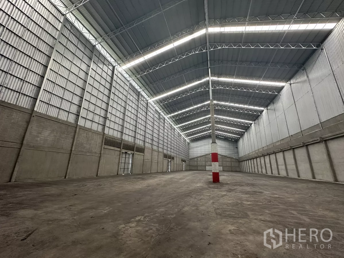 货栈 出租在Mueang Pathum Thani, Pathum Thani - 开阔仓储大厅，中央红白安全柱，金属墙面与明亮灯带。