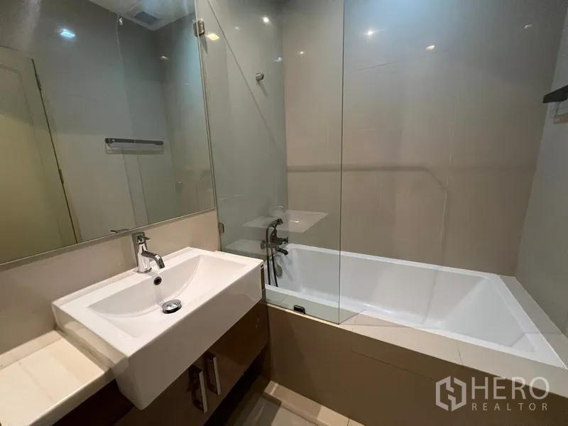 Condominium for rent or sale in Watthana, Bangkok - Bathroom with white bathtub, glass shower screen, sink and mirror