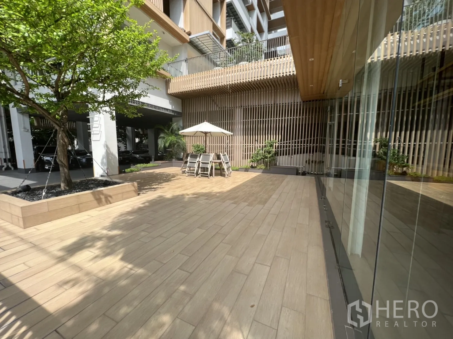 พื้นที่ขายปลีก ให้เช่าในWatthana, Bangkok - ลานกลางแจ้งปูไม้ลาย พร้อมโต๊ะร่มและหน้าร้านกระจก มีต้นไม้จัดสวน