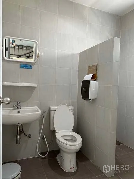 Factory for rent in Samut Prakan - Clean tiled restroom with toilet, sink and mirror inside the factory.