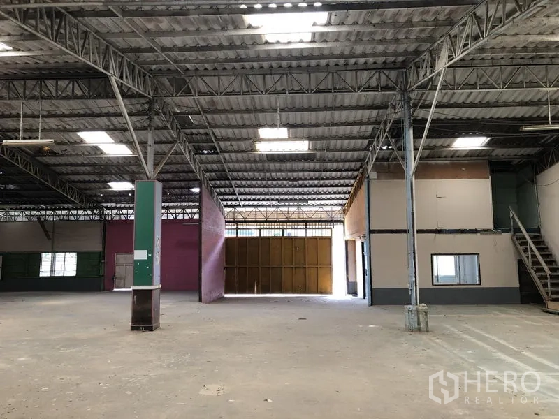 Warehouse for rent in Sai Mai, Bangkok - Warehouse hall with partitioned office, staircase to an upper room, and a large sliding entrance.