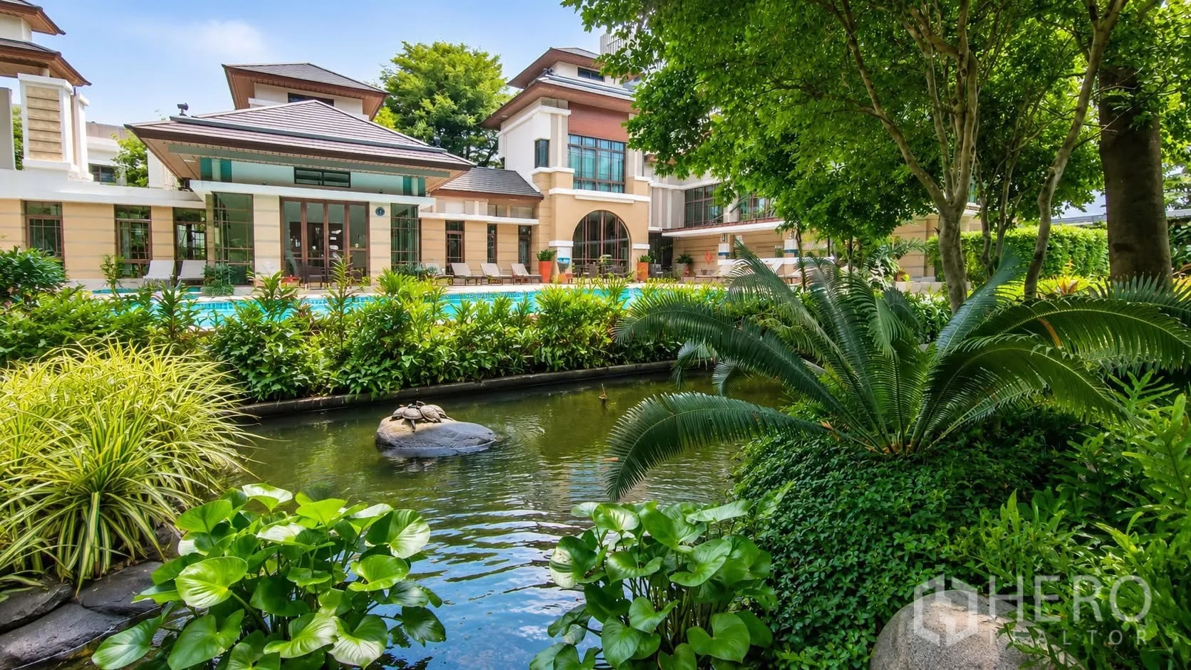 Detached House for rent in Watthana, Bangkok - Landscaped pond and greenery facing a clubhouse-style building with a swimming pool.