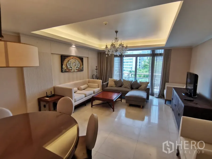 คอนโด ให้เช่าในPathum Wan, Bangkok - ห้องนั่งเล่นกว้าง เพดานหลุมติดโคมระย้า โซฟาเข้ามุม ประตูสไลด์ออกระเบียง มองเห็นต้นไม้และวิวเมือง