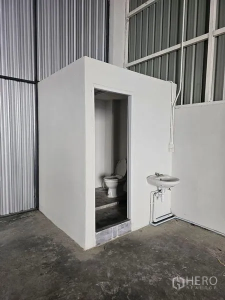 货栈 出租在Khlong Toei, Bangkok - 仓库内的独立卫生间，含坐便器与壁挂式洗手盆，水泥地面。