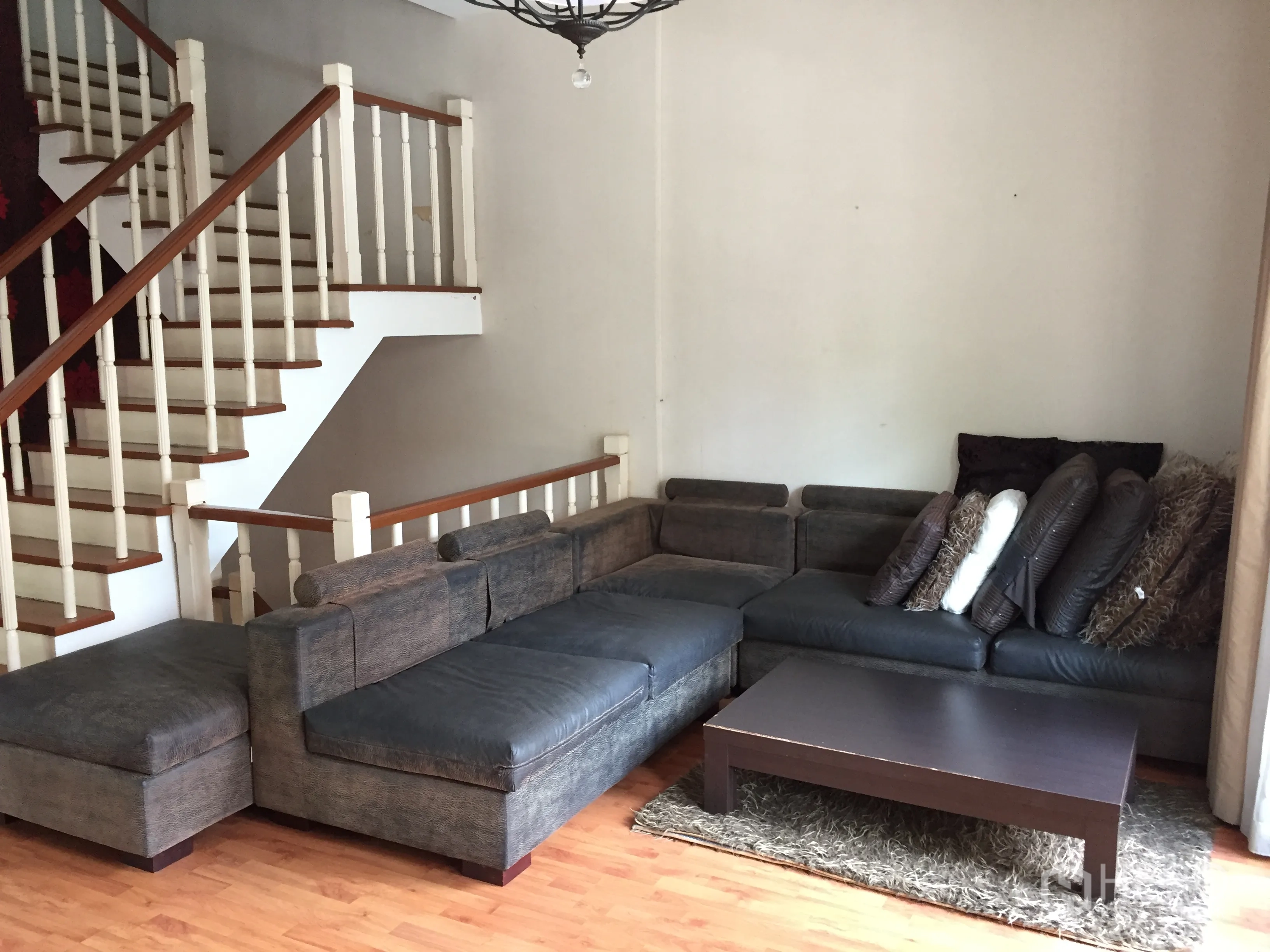 Townhouse for rent or sale in Bueng Kum, Bangkok - Living room featuring an L-shaped sectional sofa, coffee table and staircase with wooden handrails.