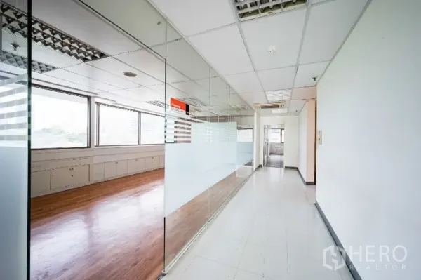 办公空间 出租在Pathum Wan, Bangkok - 明亮的办公走廊，整面玻璃隔断与磨砂贴膜，旁连木地板会议室与大窗户。