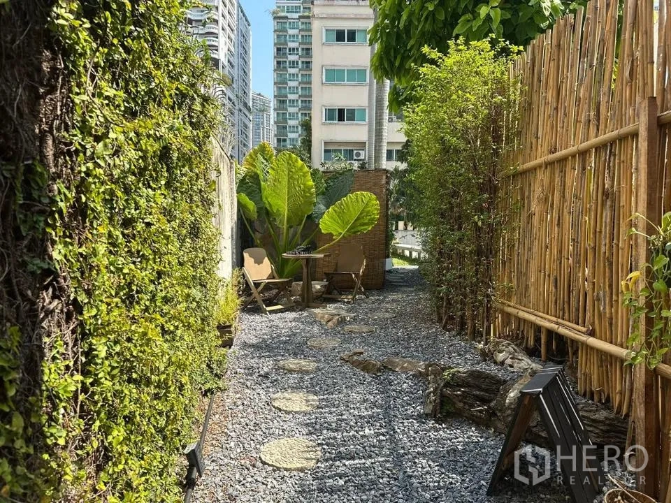 พื้นที่ขายของ for rent in Khlong Toei, Bangkok - ทางเดินโรยกรวดริมรั้วไม้ไผ่และกำแพงไม้เลื้อย เห็นต้นไม้และอาคารเมืองด้านหลัง