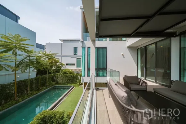 บ้าน ให้เช่าหรือขายในSaphan Sung, Bangkok - ระเบียงนั่งเล่นชมสระแบบสระยาว สนามหญ้า และบ้านสไตล์มินิมอลรอบข้าง