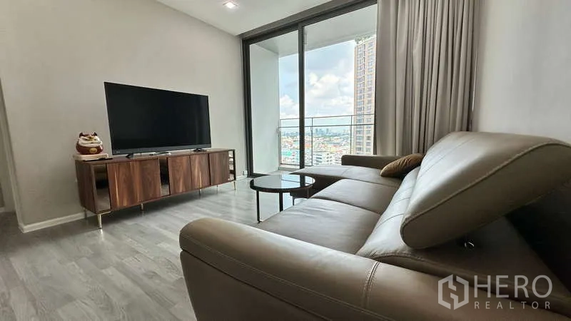 Condominium for rent - Modern living room with leather sectional, TV console, and floor-to-ceiling doors opening to a balcony with city views.