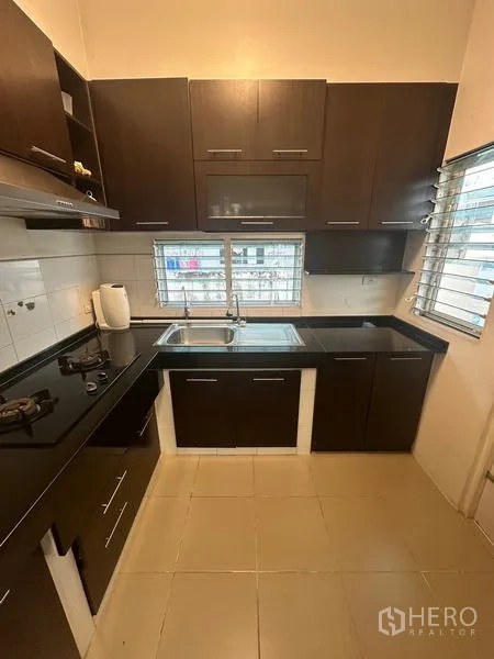 Detached House for sale in Prawet, Bangkok - Compact U-shaped kitchen with dark cabinets, gas hob and sink under windows.