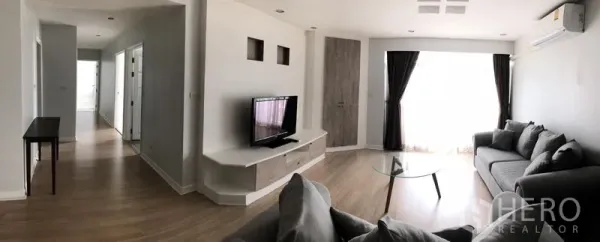 公寓 出租在Watthana, Bangkok - Royal Castle公寓明亮客厅，灰色沙发、电视柜、木地板与大窗帘落地窗。