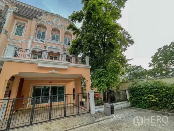 Townhouse for rent in Phasi Charoen, Bangkok - Three-storey peach townhouse with gated carport and balcony shaded by a large tree.