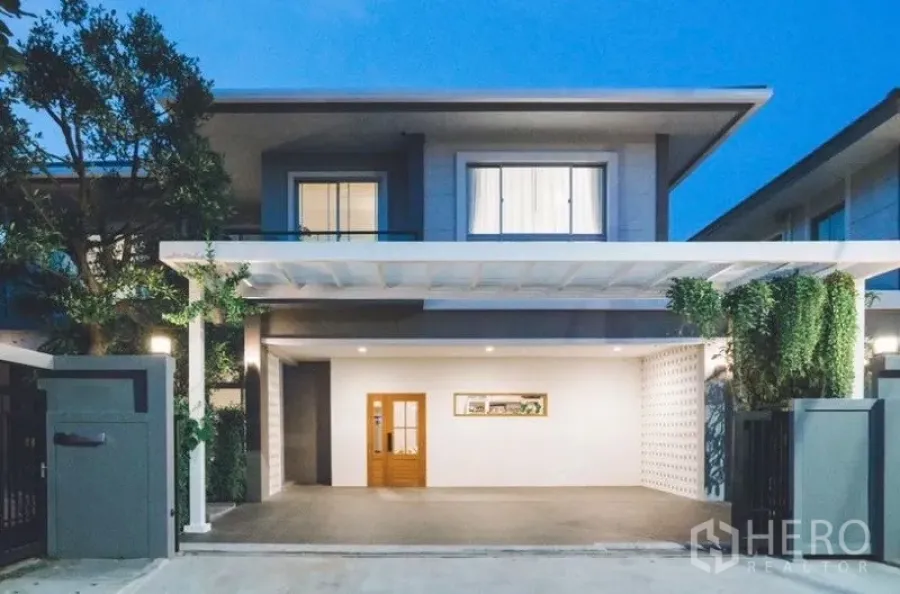 独立式住宅 出租 - 黄昏时的两层外立面，宽大车棚、木门与景观绿植。