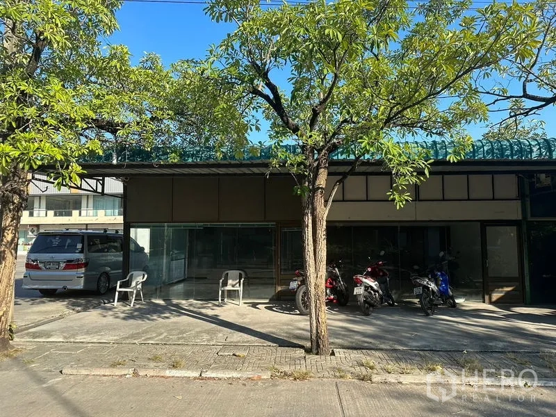 Warehouse for rent in Saphan Sung, Bangkok - Street-facing warehouse facade with glass storefront, shade trees and parking area in Saphan Sung, Bangkok.
