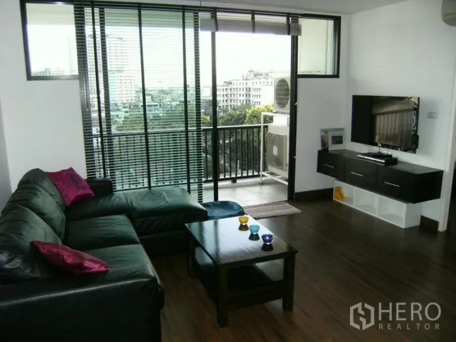 Condominium for rent in Watthana, Bangkok - Bright living room with L-shaped sofa, wall-mounted TV, and balcony overlooking the city.