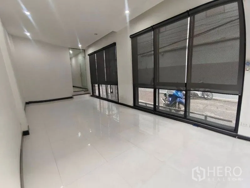 Shophouse for rent or sale in Pom Prap Sattru Phai, Bangkok - Bright ground-floor interior with glossy white tiles and large windows with roller shades.