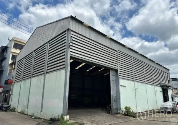 คลังสินค้า ขายในBang Bon, Bangkok - ภาพภายนอกมุมอาคาร โกดังโครงเหล็กผนังลอน มีทางเข้ารถและชายคาสูง