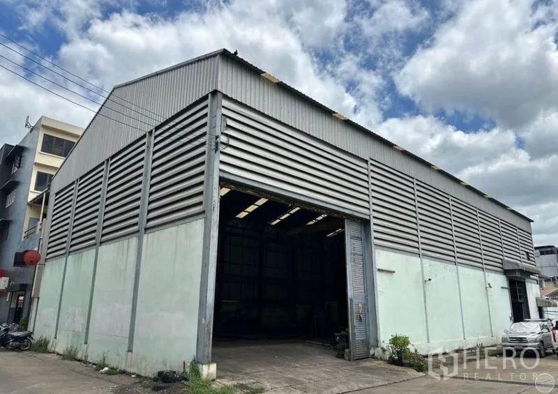 คลังสินค้า ขายในBang Bon, Bangkok - ภาพภายนอกมุมอาคาร โกดังโครงเหล็กผนังลอน มีทางเข้ารถและชายคาสูง