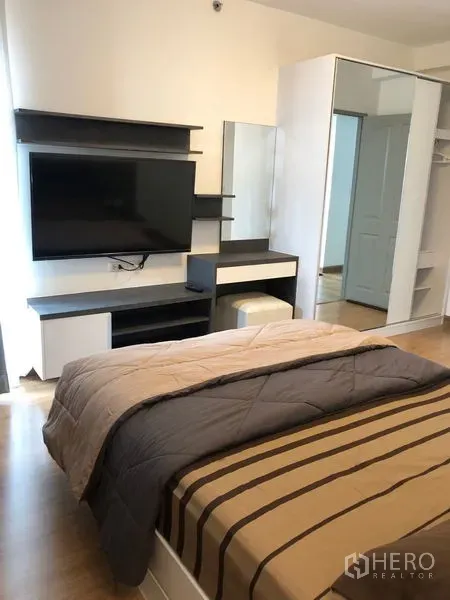 Condominium for rent in Huai Khwang, Bangkok - Cozy bedroom with TV wall, dressing table, and mirrored wardrobe beside a queen bed.