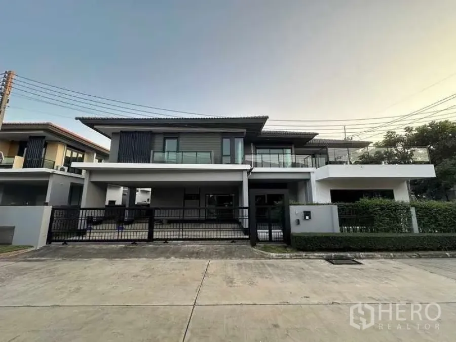 บ้าน ขายในLam Luk Ka, Pathum Thani - บ้านเดี่ยวสองชั้นสไตล์โมเดิร์น พร้อมระเบียงกว้างและรั้วหน้าบ้าน เวลาเย็นในลำลูกกา