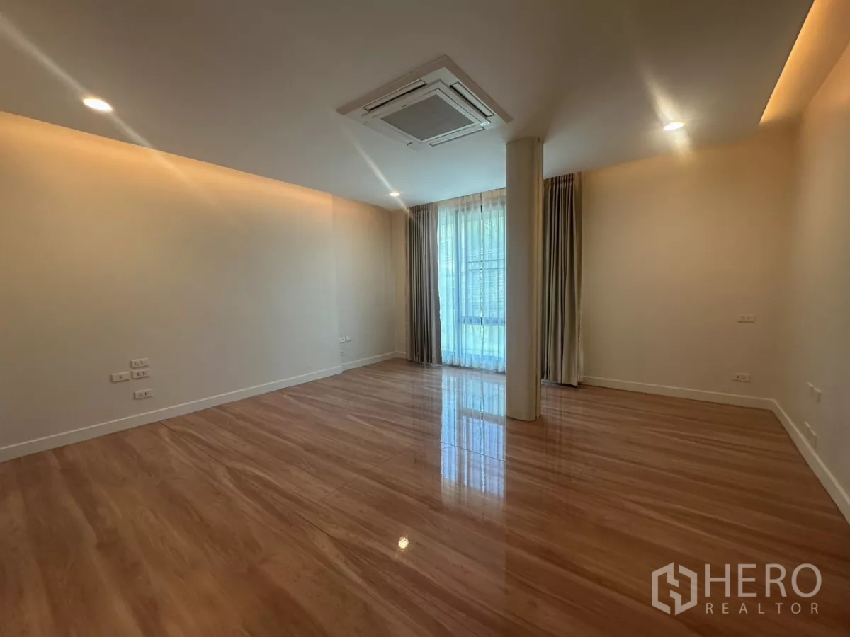 Townhouse for rent in Watthana, Bangkok - Large master bedroom with floor-to-ceiling curtains and wood floors.