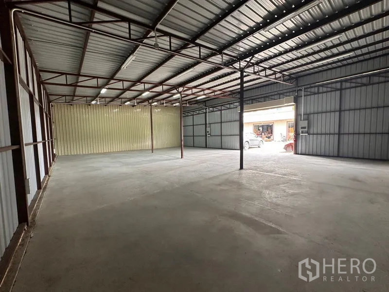 Warehouse for rent in Mueang Nonthaburi, Nonthaburi - Warehouse interior facing the loading bay with metal sheet walls, overhead lights, and vehicles visible outside.