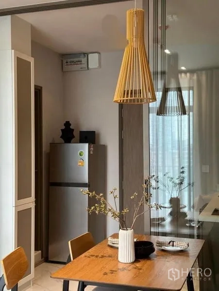 公寓 出租或出售在Watthana, Bangkok - 餐桌与木质吊灯特写，旁有不锈钢冰箱与玻璃隔断。